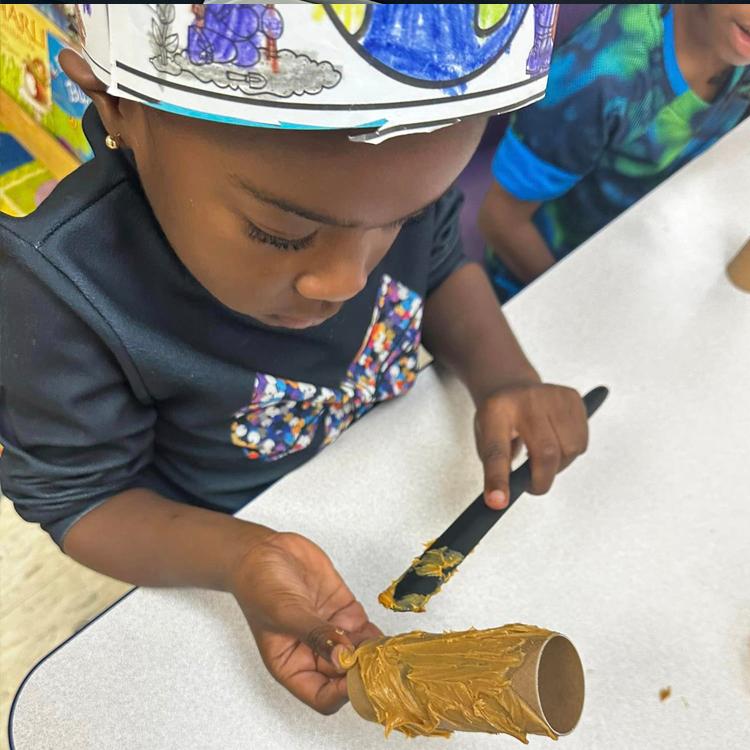 A child paints peanut butter on an Earth Day craft project for the birds