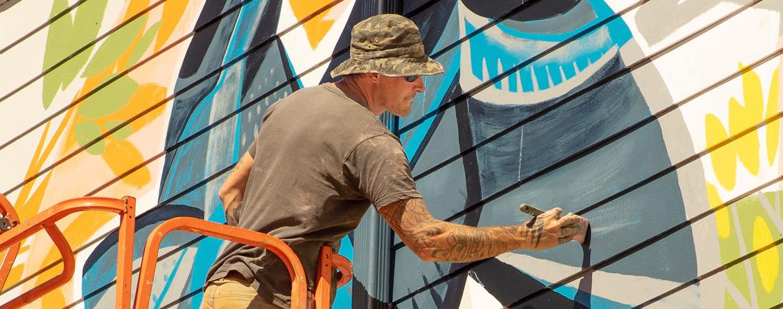 A painter creates a colorful mural with bold strokes of paint on a big wall